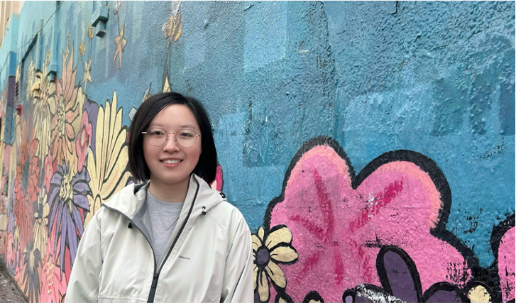 Sitong Wang standing in front of a wall painted with street art