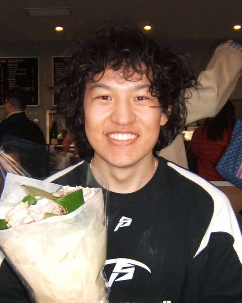 Ben Yang, smiling, holds a bouquet of flowers wrapped in paper.