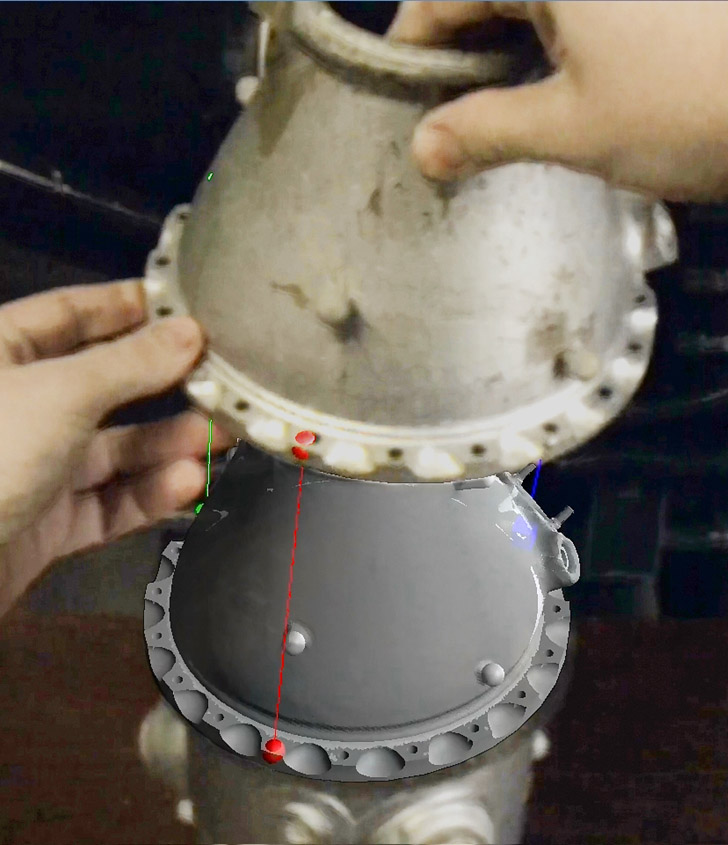 A maintenance technician's view through a see-through head-worn display
    of augmented reality instructions for assembling an aircraft engine combustion chamber. A remote expert demonstrates how
    to place a virtual copy of the chamber top, while the technician holds the real chamber top and moves it into place,
    guided by colored rubber-band lines.